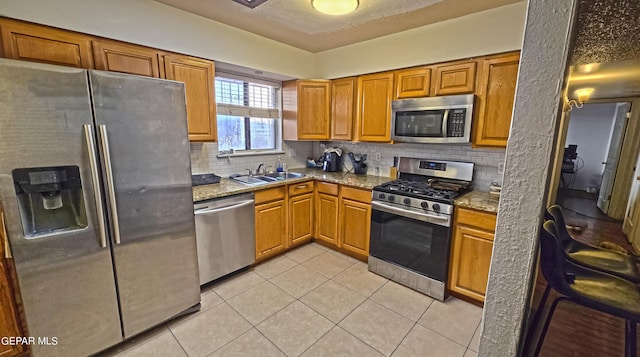 kitchen with appliances with stainless steel finishes, tasteful backsplash, light stone counters, sink, and light tile patterned flooring