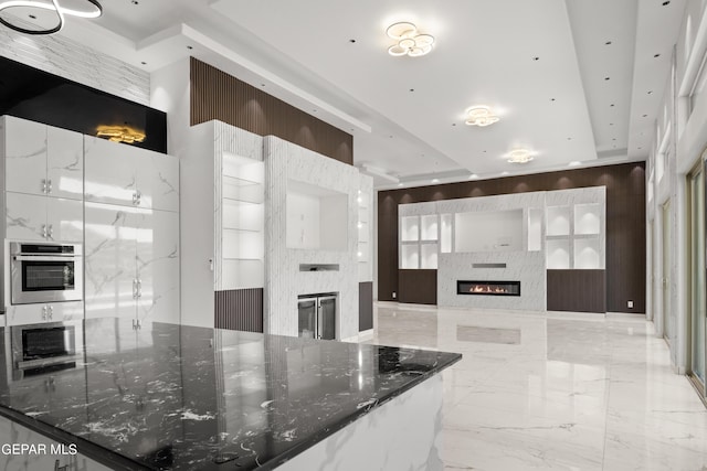 kitchen with white cabinetry, stainless steel oven, a stone fireplace, wood walls, and dark stone counters