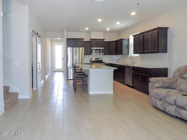 kitchen with dark brown cabinetry, sink, a center island, a breakfast bar area, and appliances with stainless steel finishes