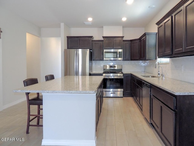 kitchen with a kitchen bar, decorative backsplash, stainless steel appliances, sink, and a center island