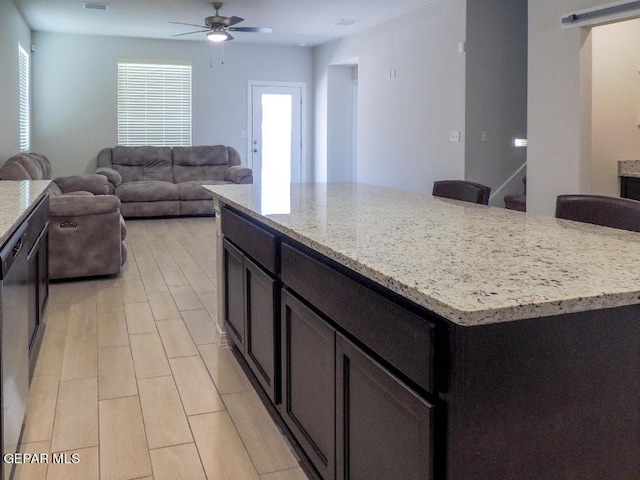 kitchen with a kitchen bar, stainless steel dishwasher, ceiling fan, a kitchen island, and light stone counters