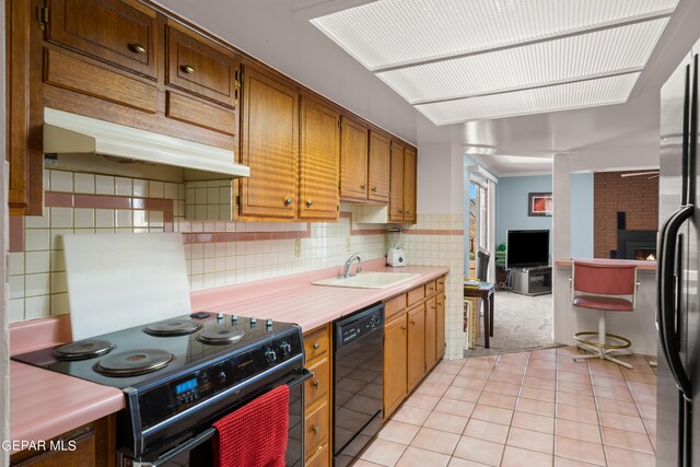 kitchen featuring a fireplace, light tile flooring, black appliances, backsplash, and sink