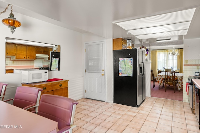 kitchen with brown cabinetry, white microwave, fridge with ice dispenser, stainless steel range with electric stovetop, and light tile patterned flooring