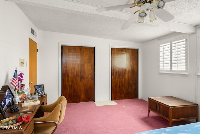 carpeted bedroom with a textured ceiling, two closets, visible vents, and a ceiling fan