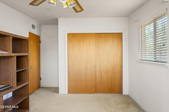 carpeted bedroom with a ceiling fan, a closet, visible vents, and a textured ceiling