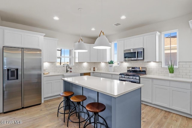 kitchen featuring white cabinets, pendant lighting, a kitchen island, and stainless steel appliances