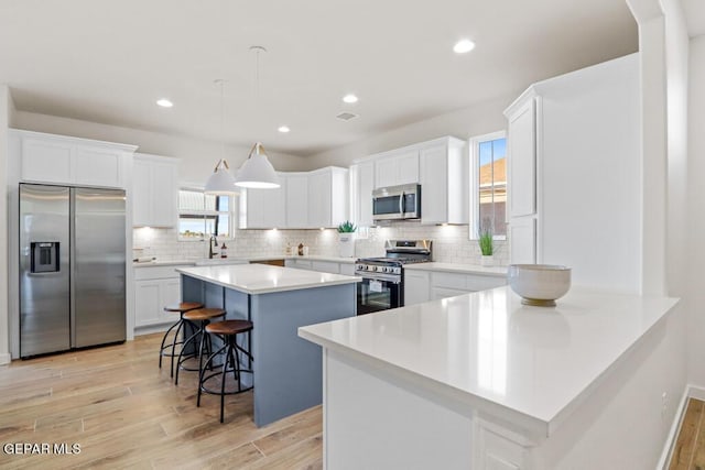 kitchen with white cabinetry, a center island, stainless steel appliances, pendant lighting, and a kitchen bar