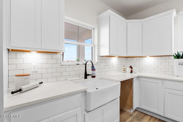 kitchen with backsplash, light hardwood / wood-style floors, white cabinetry, and sink