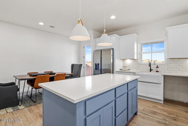 kitchen with pendant lighting, white cabinets, sink, stainless steel fridge, and tasteful backsplash