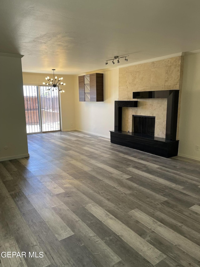 unfurnished living room featuring track lighting, crown molding, an inviting chandelier, hardwood / wood-style floors, and a tiled fireplace