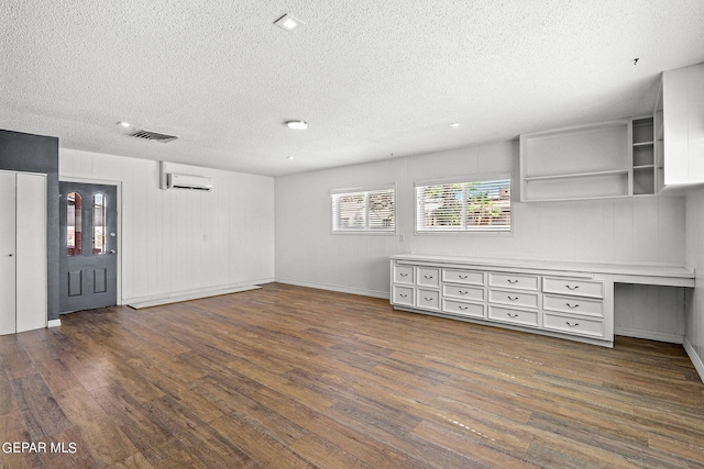 interior space featuring a textured ceiling, built in desk, a wall unit AC, and dark wood-type flooring