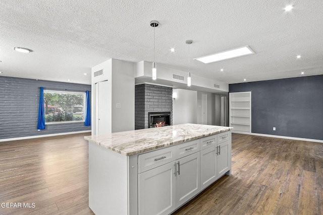 kitchen featuring hanging light fixtures, a brick fireplace, a kitchen island, dark hardwood / wood-style flooring, and white cabinetry