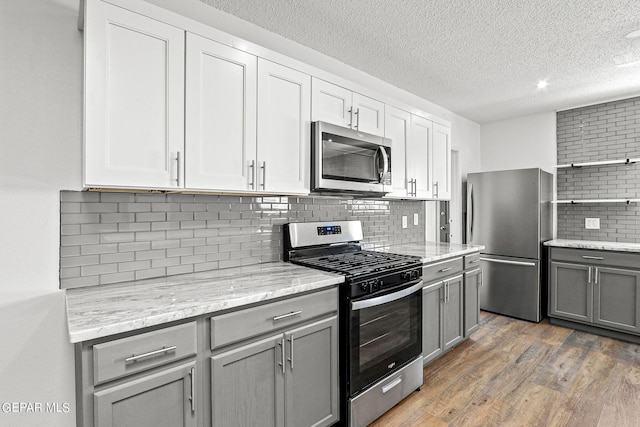 kitchen featuring dark hardwood / wood-style floors, gray cabinets, a textured ceiling, appliances with stainless steel finishes, and tasteful backsplash