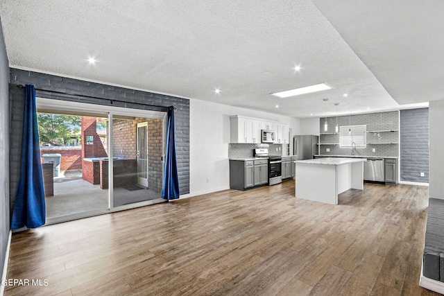 kitchen with a skylight, light hardwood / wood-style floors, a textured ceiling, appliances with stainless steel finishes, and a kitchen island