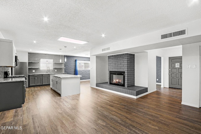 kitchen with a skylight, a brick fireplace, pendant lighting, gray cabinets, and a kitchen island