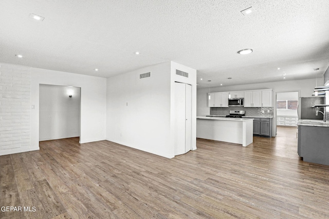 unfurnished living room featuring a textured ceiling, light hardwood / wood-style floors, and sink