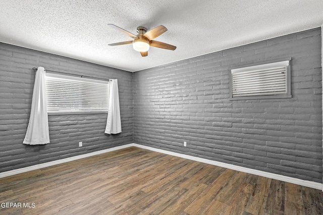 spare room featuring ceiling fan, dark hardwood / wood-style flooring, a textured ceiling, and brick wall