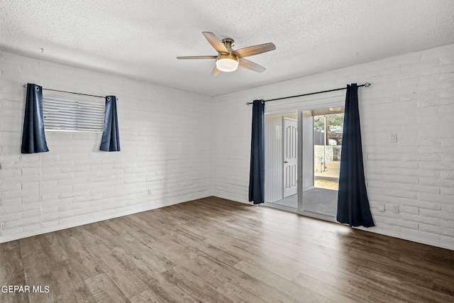 spare room featuring hardwood / wood-style floors, ceiling fan, and brick wall