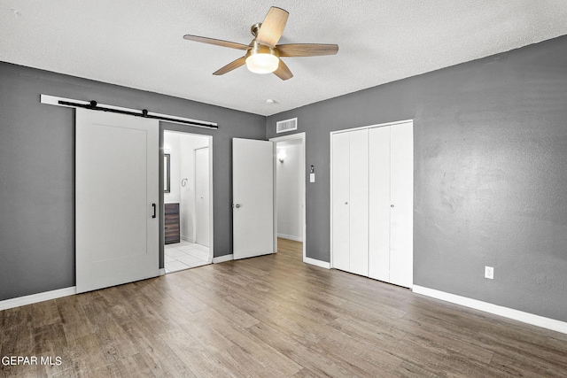 unfurnished bedroom featuring ceiling fan, a barn door, a textured ceiling, light hardwood / wood-style floors, and a closet