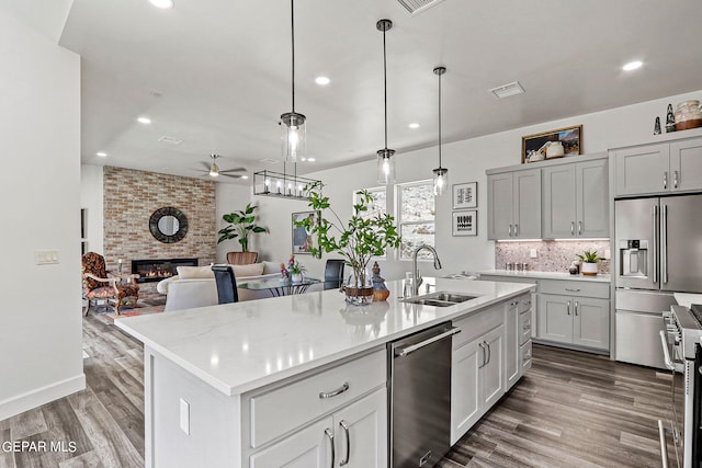 kitchen with stainless steel appliances, a kitchen island with sink, ceiling fan, decorative light fixtures, and a fireplace