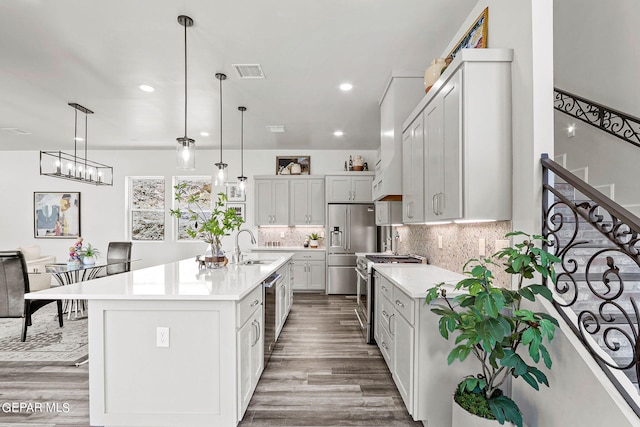 kitchen featuring tasteful backsplash, stainless steel appliances, wood-type flooring, decorative light fixtures, and an island with sink