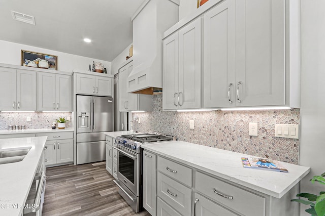 kitchen with decorative backsplash, light stone countertops, premium range hood, dark wood-type flooring, and high quality appliances