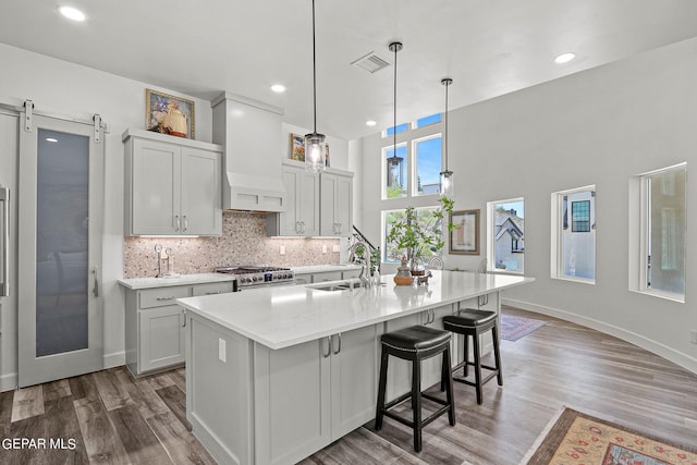 kitchen with a center island with sink, a barn door, wood-type flooring, and high end stainless steel range oven