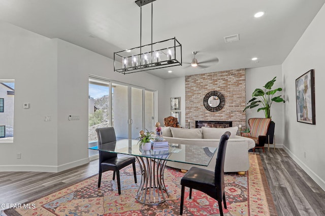 dining room with wood-type flooring, a brick fireplace, and ceiling fan