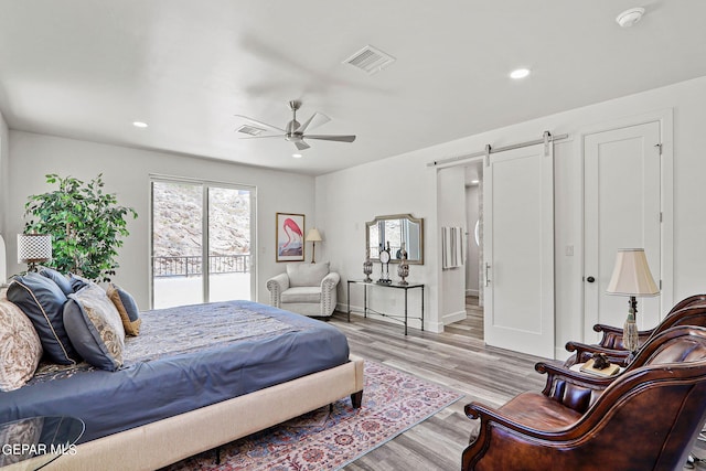 bedroom with ceiling fan, a barn door, access to exterior, and light hardwood / wood-style flooring