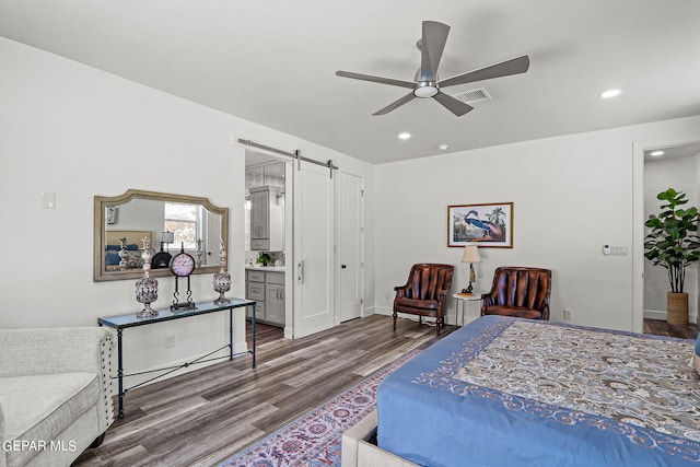 bedroom featuring a barn door, ceiling fan, ensuite bath, and wood-type flooring