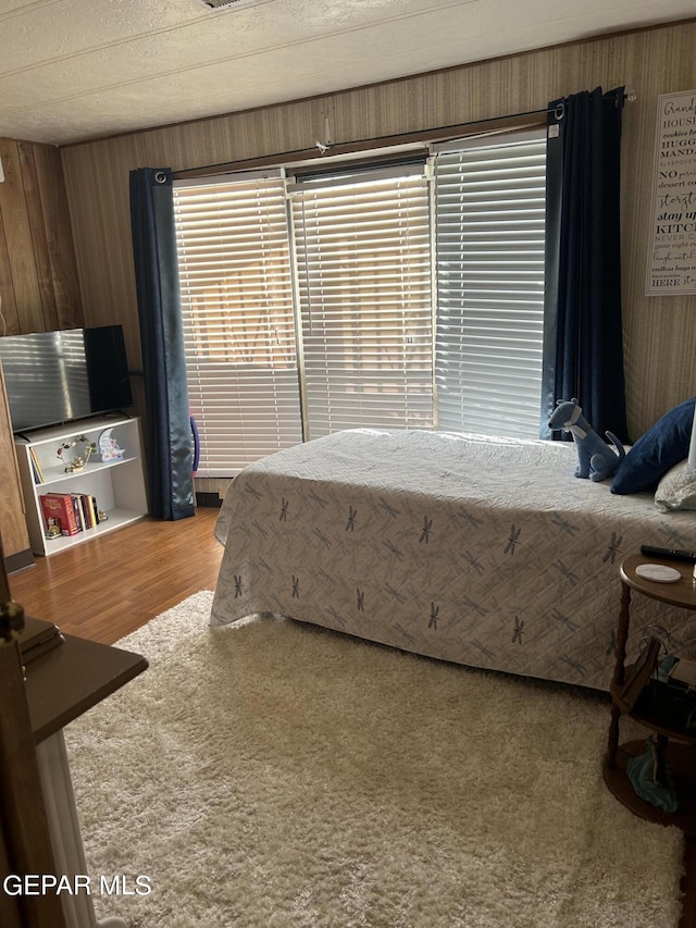 bedroom featuring a textured ceiling, multiple windows, and wooden walls