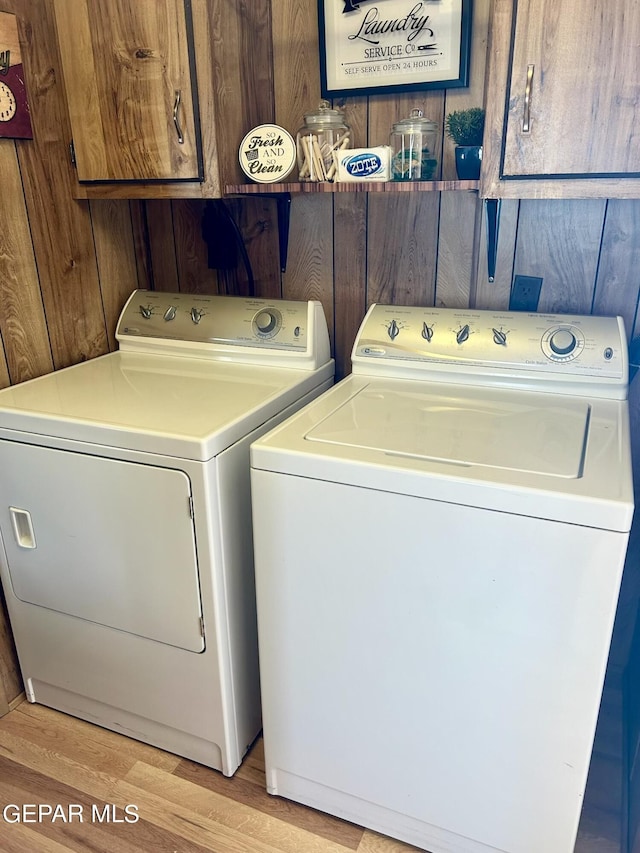 washroom featuring washer and dryer, cabinets, wood walls, and light wood-type flooring