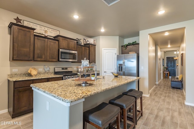 kitchen with dark brown cabinets, stainless steel appliances, a kitchen island with sink, and sink