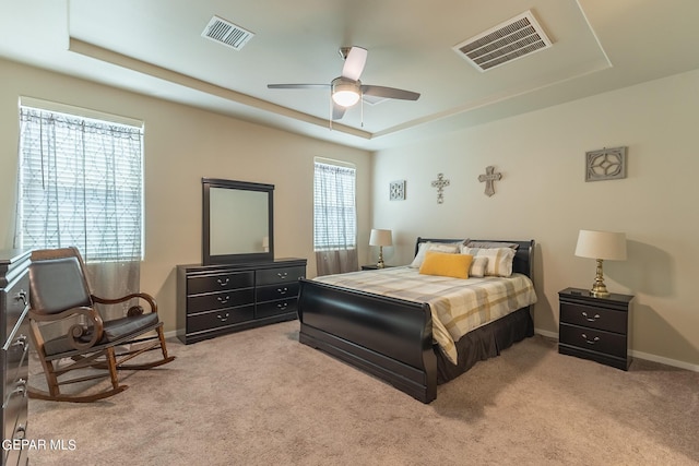 bedroom with a tray ceiling, multiple windows, ceiling fan, and light carpet