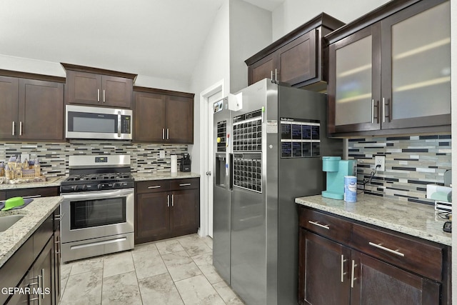 kitchen with decorative backsplash, appliances with stainless steel finishes, dark brown cabinetry, and light stone countertops