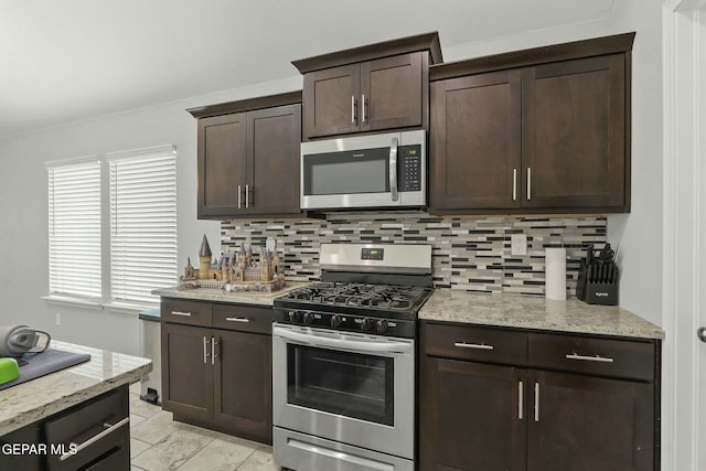 kitchen with appliances with stainless steel finishes, dark brown cabinetry, light stone counters, and backsplash