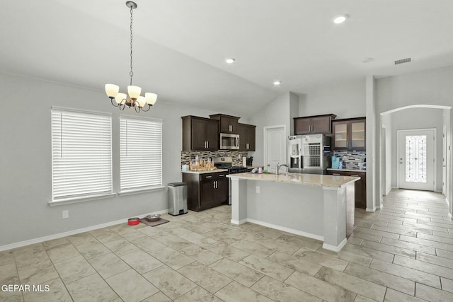 kitchen featuring lofted ceiling, backsplash, a kitchen island with sink, appliances with stainless steel finishes, and decorative light fixtures