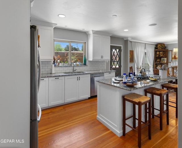 kitchen featuring appliances with stainless steel finishes, a sink, light stone counters, and white cabinets