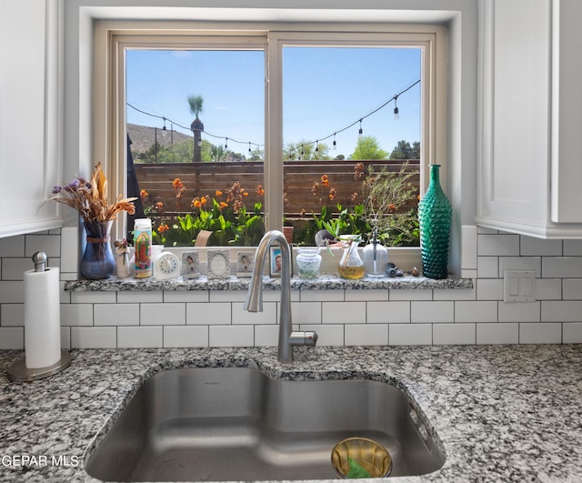 kitchen with white cabinets, light stone countertops, decorative backsplash, and a sink