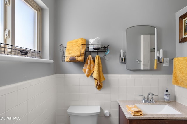 bathroom with tile walls, wainscoting, vanity, and toilet