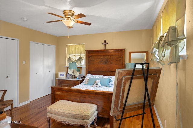 bedroom featuring two closets, a ceiling fan, baseboards, and dark wood-type flooring