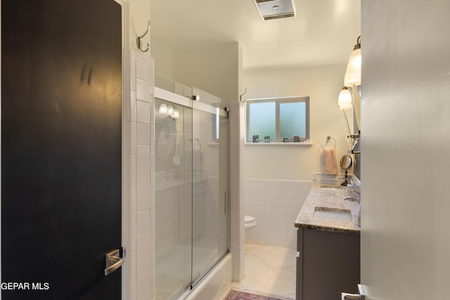 bathroom featuring shower / bath combination with glass door, tile walls, toilet, a sink, and tile patterned floors