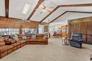 carpeted living room with plenty of natural light, vaulted ceiling with beams, ceiling fan, and wood walls