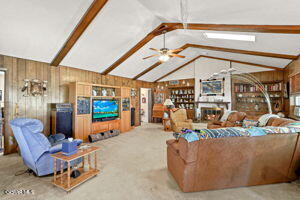 living room featuring vaulted ceiling with beams, wooden walls, and ceiling fan