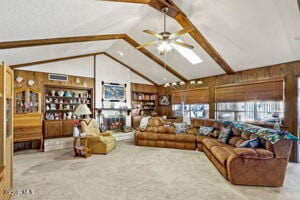 living room with vaulted ceiling with beams, wooden walls, and ceiling fan