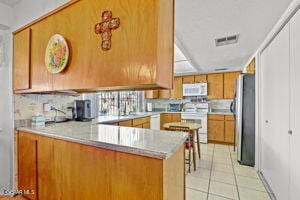 kitchen with light tile patterned floors, stainless steel fridge, range, decorative backsplash, and kitchen peninsula