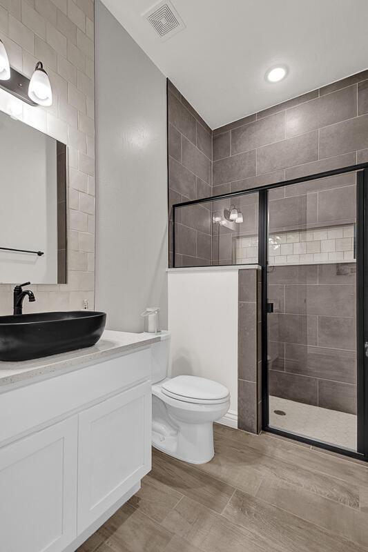 bathroom featuring a shower with door, vanity, and toilet