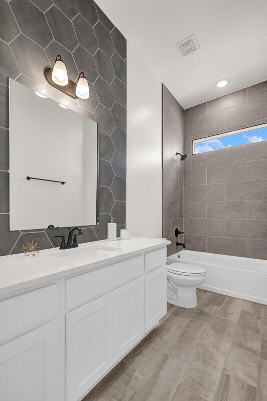 full bathroom with vanity, toilet, tiled shower / bath combo, and tile walls