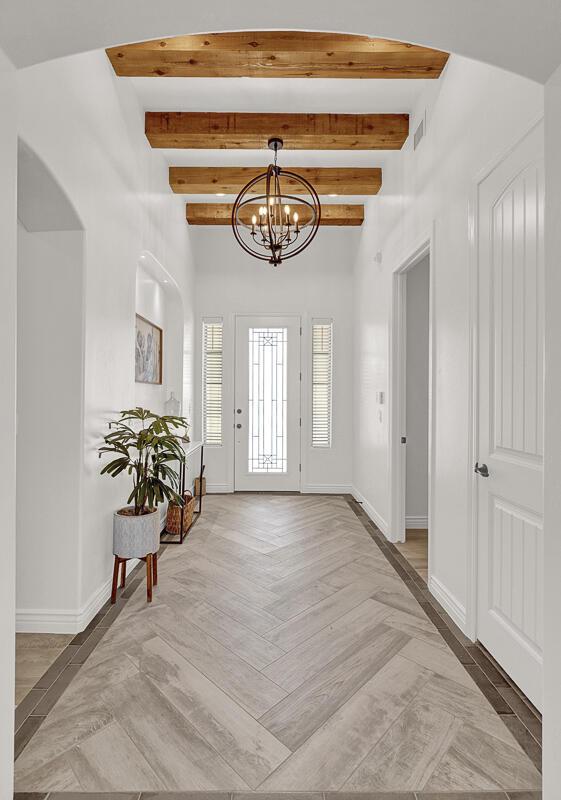 foyer entrance featuring beam ceiling, light parquet floors, and a chandelier