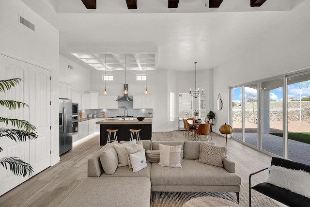 living room featuring coffered ceiling, light hardwood / wood-style flooring, a notable chandelier, beam ceiling, and a high ceiling